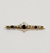 Gold coloured metal and garnet bar brooch set three garnets with pierced and twisted bar pattern