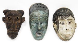 Three ethnic wooden carved face masks, one with mottled blue finish and another with a white finish,