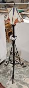 Wrought iron standard lamp with scrolling supports and three splayed legs, having a Tiffany-style
