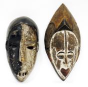 Two ethnic carved wooden face masks, one with half white painted face, possibly Democratic