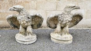 Pair of composite stone garden statues in the form of opposing eagles, wings displayed, on oval