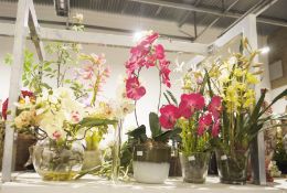 Five faux floral displays four contained within glass vases the other in a ceramic pot predominantly