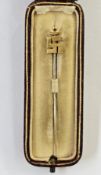 Gold-coloured stickpin decorated with a Buddhist symbol, registration number to reverse