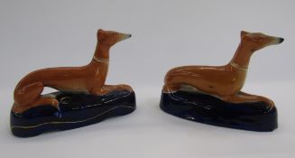 Pair of Staffordshire pottery greyhound pen rests, each ochre coloured hound seated on a dark blue