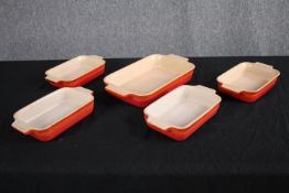 A collection of four Le Creuset baking dishes in the classic orange finish. L.31 W.28cm. (largest)