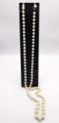 A long knotted string of graduated cultured pearls with 9ct yellow gold red stone set hook and