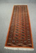 A Bokhara runner with repeating gul motifs on a terracotta ground. L.245 W.80cm.