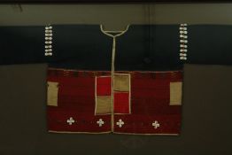 † A framed and glazed Burmese woven wool and cotton tunic with cowrie shell detailing. H.79 W.152cm.