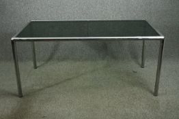 A contemporary dining table with smoked glass top in two sections raised on chromed supports. H.71