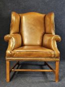 A George III style oak wingback armchair, with studded tan leather upholstery, 20th century.