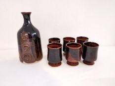 A sake bottle and six cups with black and brown glaze by A. J. Maseid, Bletchley pottery. Label on