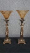 A pair of Art Deco style moulded table lamps with figural stems supporting peach glass shades. H.
