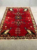 A handwoven Qashqai carpet with central stylised medallions on a burgundy field with figurehead
