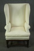 A Georgian high back wing armchair on mahogany stretchered supports resting on brass casters. H.