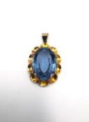 A 14 carat yellow gold floral design pendant set with an oval mixed cut synthetic blue spinel. The