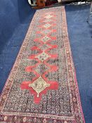 An Eastern woollen hall runner with repeating stylised lozenge medallions on a burgundy ground. L.
