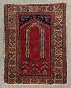 A Turkish prayer rug on a burgundy ground within stylised borders. L.119 W.94cm