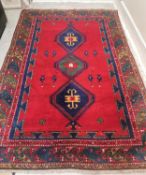 A Kazak carpet with triple lozenge medallions on a burgundy ground within stylised foliate
