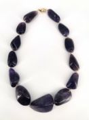 An amethyst necklace formed of thirteen graduating stones, strung on thread with yellow metal