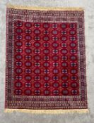 A silk Turkoman carpet with repeating flowerhead motifs on a burgundy field within stylised multiple