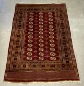 A Bokhara carpet with repeating gul medallions on a burgundy ground within multiple geometric