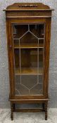 An early 20th century oak narrow display cabinet/bookcase, with a carved top rail on stretchered