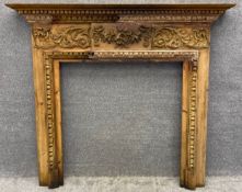A Georgian style pine fire surround with carved dentil moulding and foliate gesso decorated
