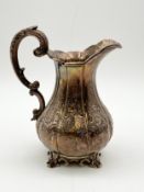 A silver baluster shaped four footed milk jug with embossed foliate design and a scrolling handle.