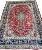 A large Persian hand woven kerman rug with an all over foliate design on a red field with a