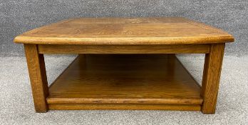 A vintage two tiered oak coffee table with a shaped top and two pull out slides on each side, on