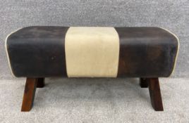 A brown leather and beige calico pommel horse style bench or foot rest on splayed wooden supports.