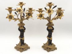 A pair of gilt metal three sconce candelabras with cherub supports holding aloft lilies standing