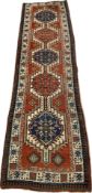 A Kazak runner with repeating hooked medallions on a burgundy ground within stylised foliate