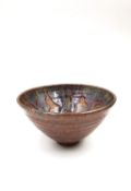 A small stoneware studio pottery bowl with a drip glazed interior on a narrow foot, with maker's