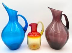 A collection of three hand blown coloured glass pitchers, two in the manner of Blenko. H.37cm (