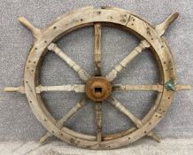 An antique weathered teak ship's wheel with eight turned spokes, a cast iron central movement, and a