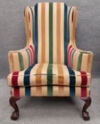 A large Georgian style wing back armchair, upholstered in striped fabric, on short cabriole supports