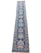 A large handmade Caucasian runner with repeating stylised hooked medallions on a sapphire ground