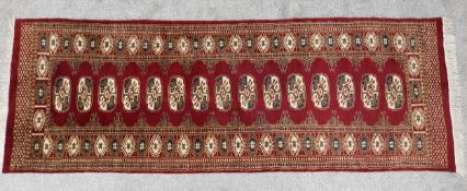 A Bokhara style runner with repeating gul medallions on a burgundy field within stylised borders.
