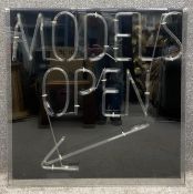A vintage neon 'Models Open' sign mounted with black background in a perspex box, from God's Own