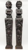 A pair of stained pine terms or pilasters carved with male and female busts over naturalistic