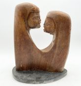 A mid-century carved teak figure group, two heads in shawls, by Robert De Quin, on a shaped slate