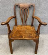 A 19th century country oak elbow chair with a carved splat flanked by scrolling side rails with