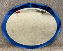 A mid-century mirror with a bevelled oval plate on a bevelled blue glass mirrored backing in the