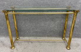 A mid-century Hollywood Regency style brass console table with a plate glass top on four stretchered
