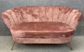 A contemporary sofa upholstered in dusty pink brushed velvet with a scalloped back on splayed