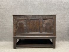 An 18th century oak coffer with a later hinged lid and a carved top rail over a central panel inlaid