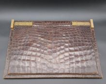An early to mid 20th century crocodile skin desk pad hinged on a decorative brass chain with a