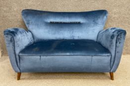 A mid-century blue brushed velvet two seater sofa having a flared back with a row of black buttons