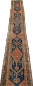 A very long Persian silk runner with repeating stylised geometric medallions over a dark blue